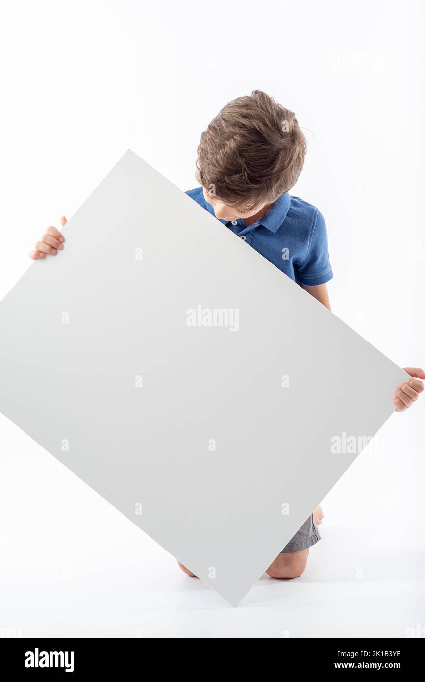 Kaukasischer Junge, der ein weißes Plakat mit Platz für Text und weißem Hintergrund hält und anschaut. Stockfoto