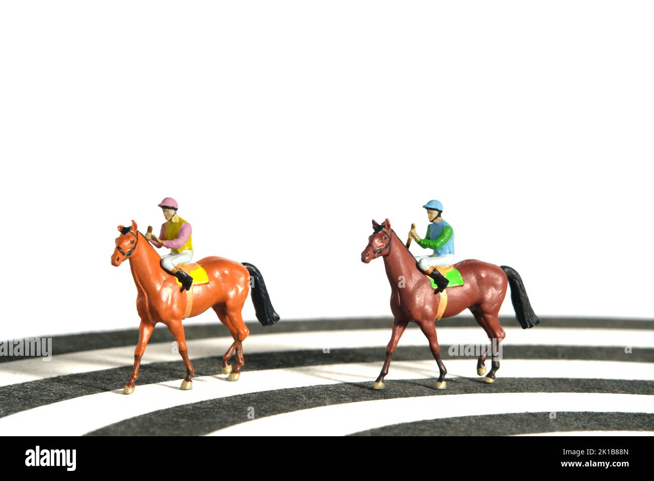 Miniatur Menschen Spielzeug Figur Fotografie. Jockey Männer reiten auf einer Rennstrecke von Dartboard. Isoliert auf weißem Hintergrund. Bildfoto Stockfoto