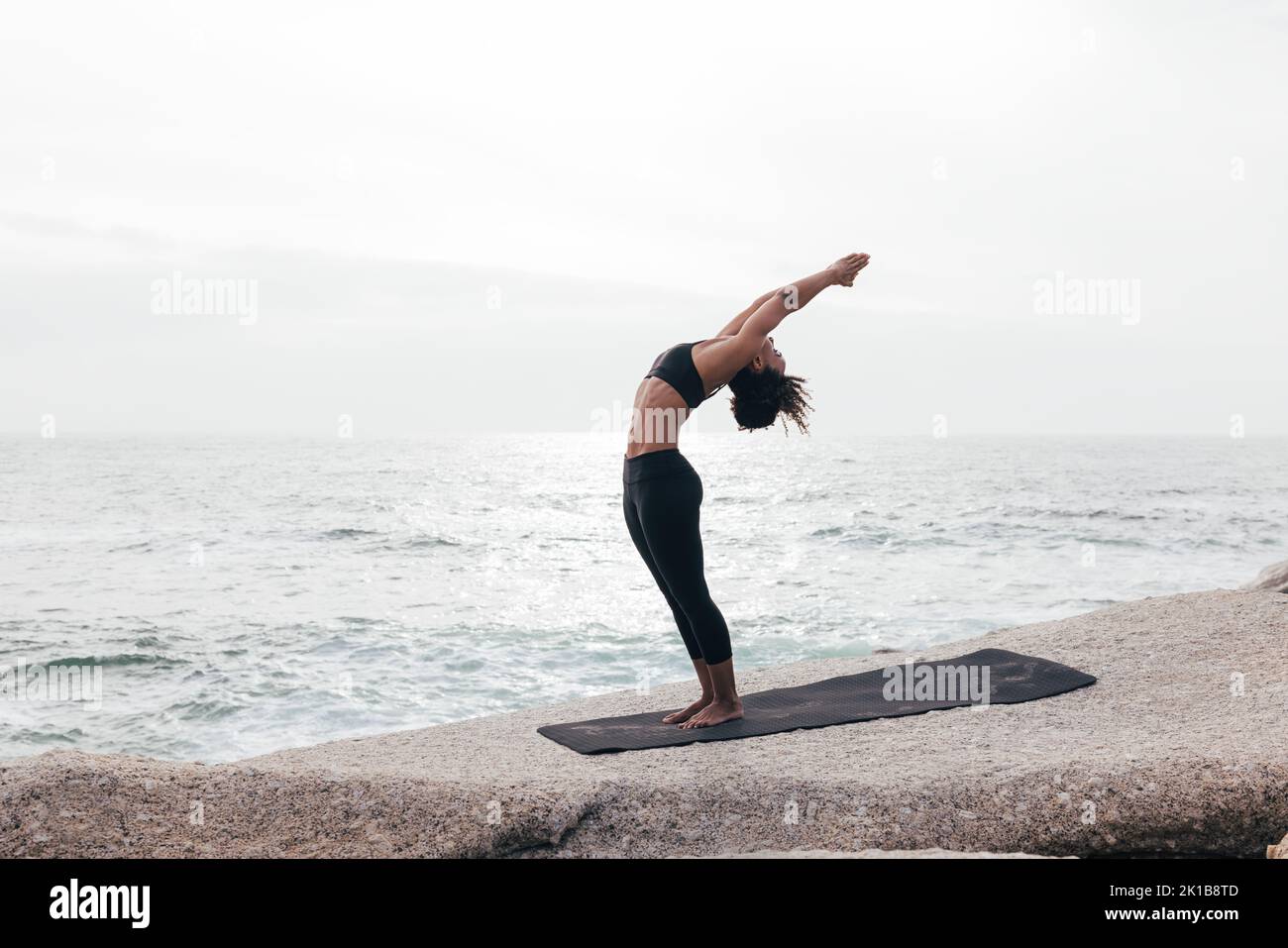 Frau in stehender Hinterbeine-Pose am Ozean Stockfoto