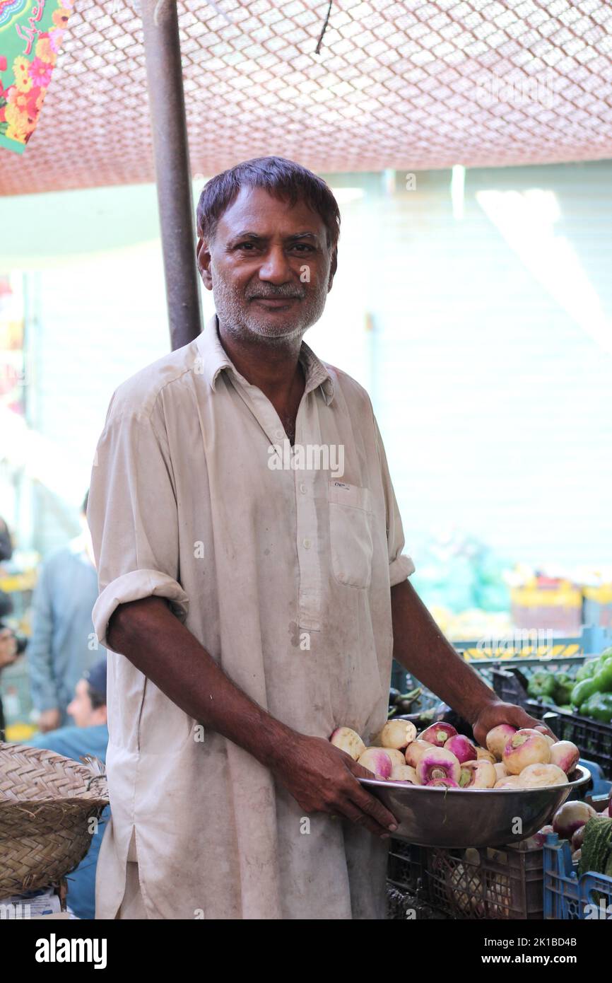 Eine vertikale Aufnahme eines pakistanischen Mannes, der auf einem Markt Früchte in einem Schalwar-Kameez verkauft Stockfoto