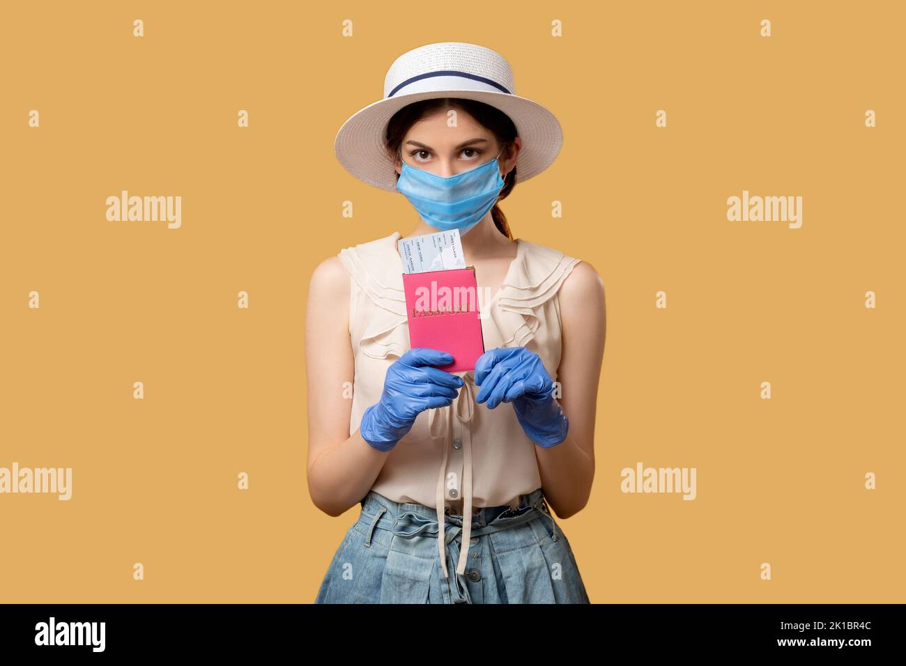 Urlaubsreise. Reisebeschränkungen. Covid-19 Urlaub. Frau in Schutzmaskenhandschuhen mit ausweisen, die die Kamera isoliert auf beige betrachten. Stockfoto