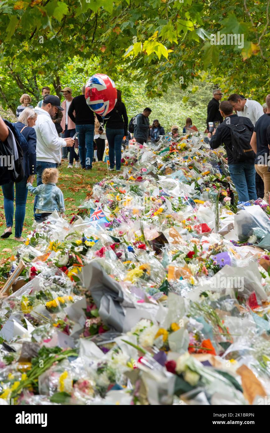 Menschen lesen Botschaften mit Blumen im Green Park nach dem Tod von Königin Elizabeth II. Blumensträuße mit Kunststoffverpackung im Park angelegt Stockfoto