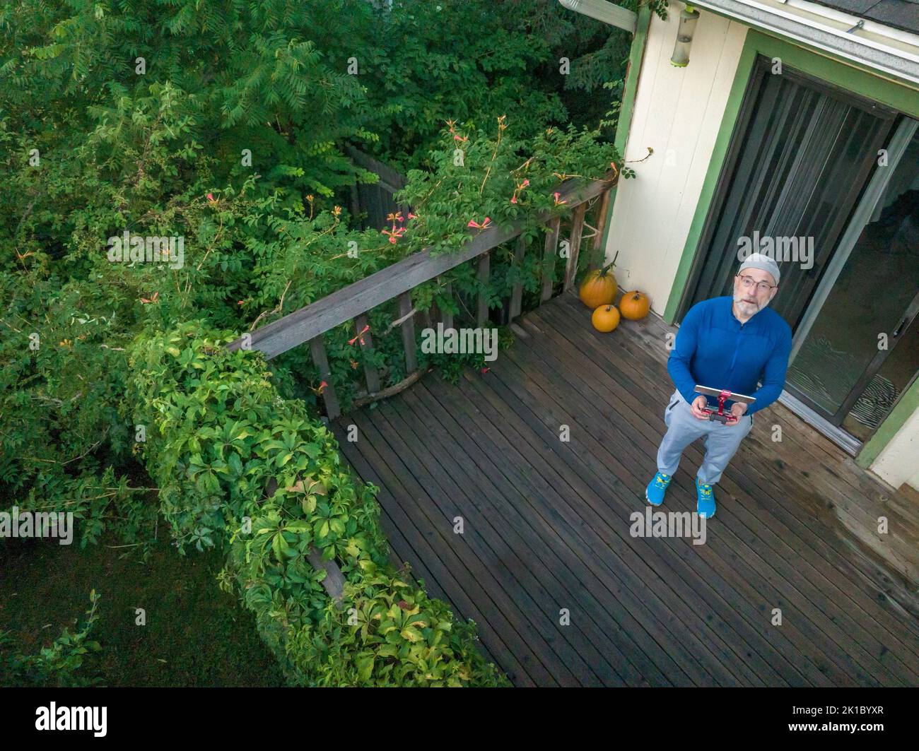 Älterer Mann mit einem Drohnenfunkcontroller und Tablet am Morgen auf seiner Hinterhofterrasse, Luftaufnahme Stockfoto