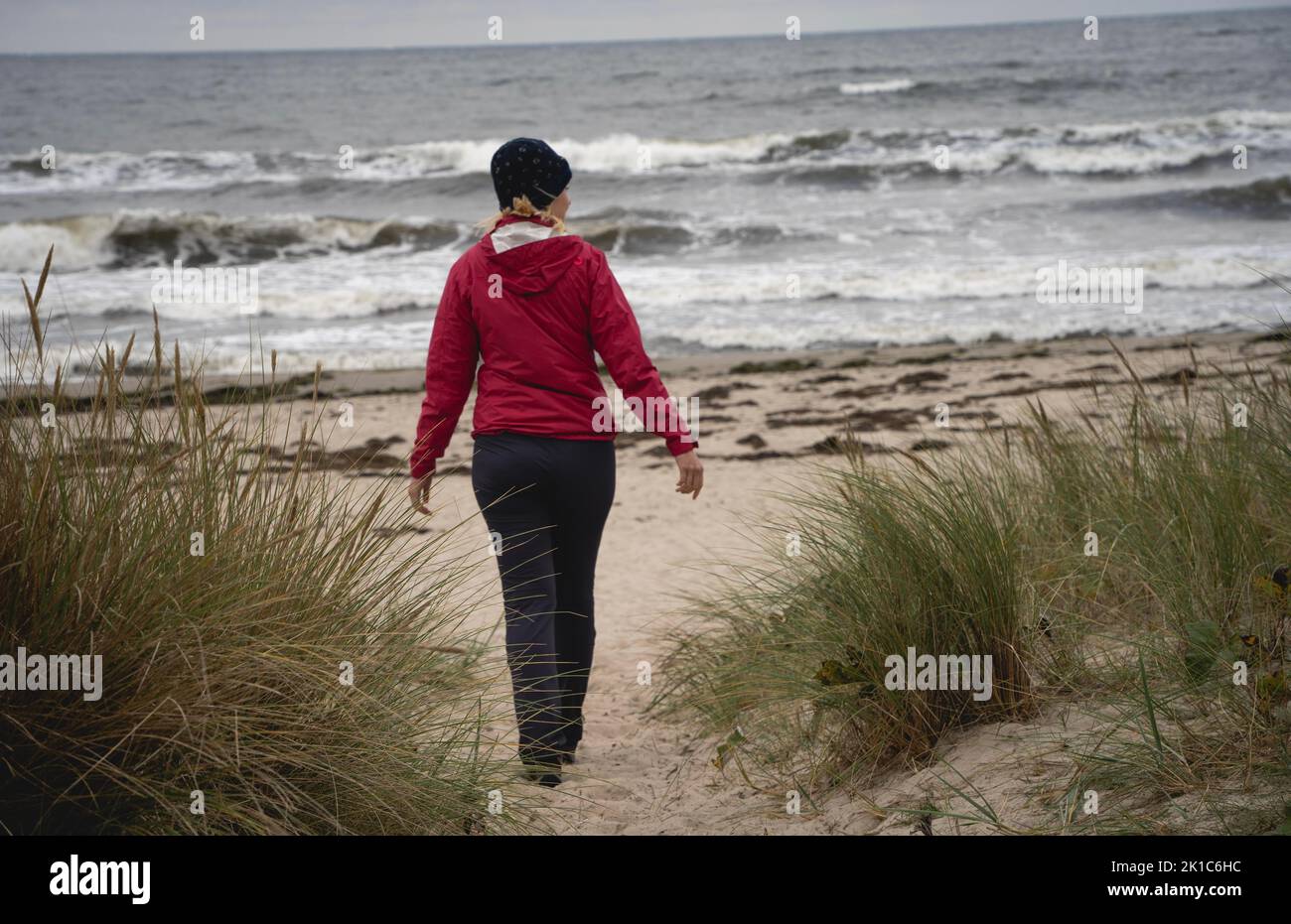 Frau in Rot beim Spaziergang am Sandstrand an der Ostsee bei düsterem Wetter, Insel Rügen, Deutschland Stockfoto