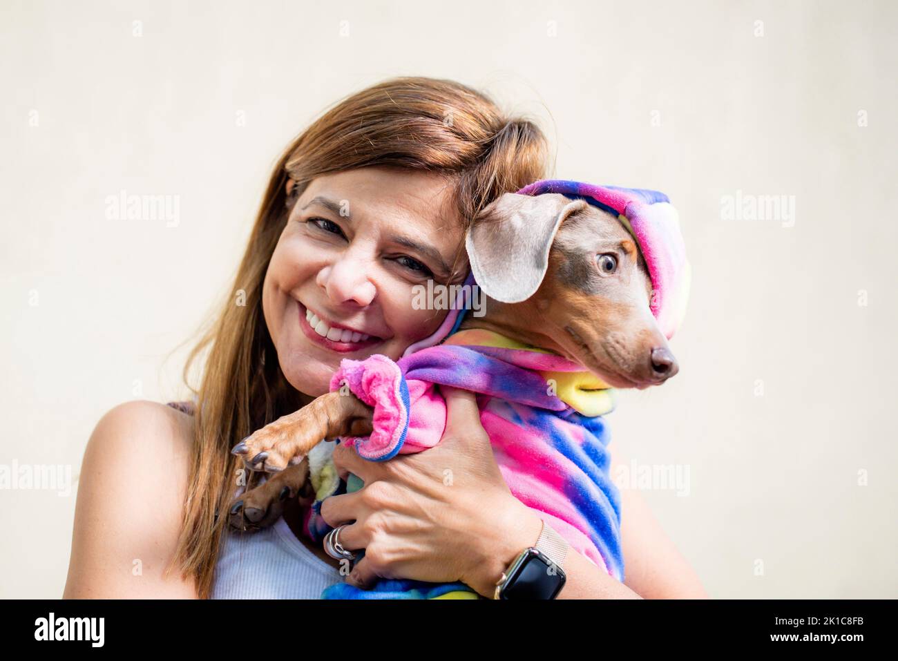 Eine lateinische Frau, die ihren Hund in beiden Kleidern hält. Sie schaut in die Kamera Stockfoto