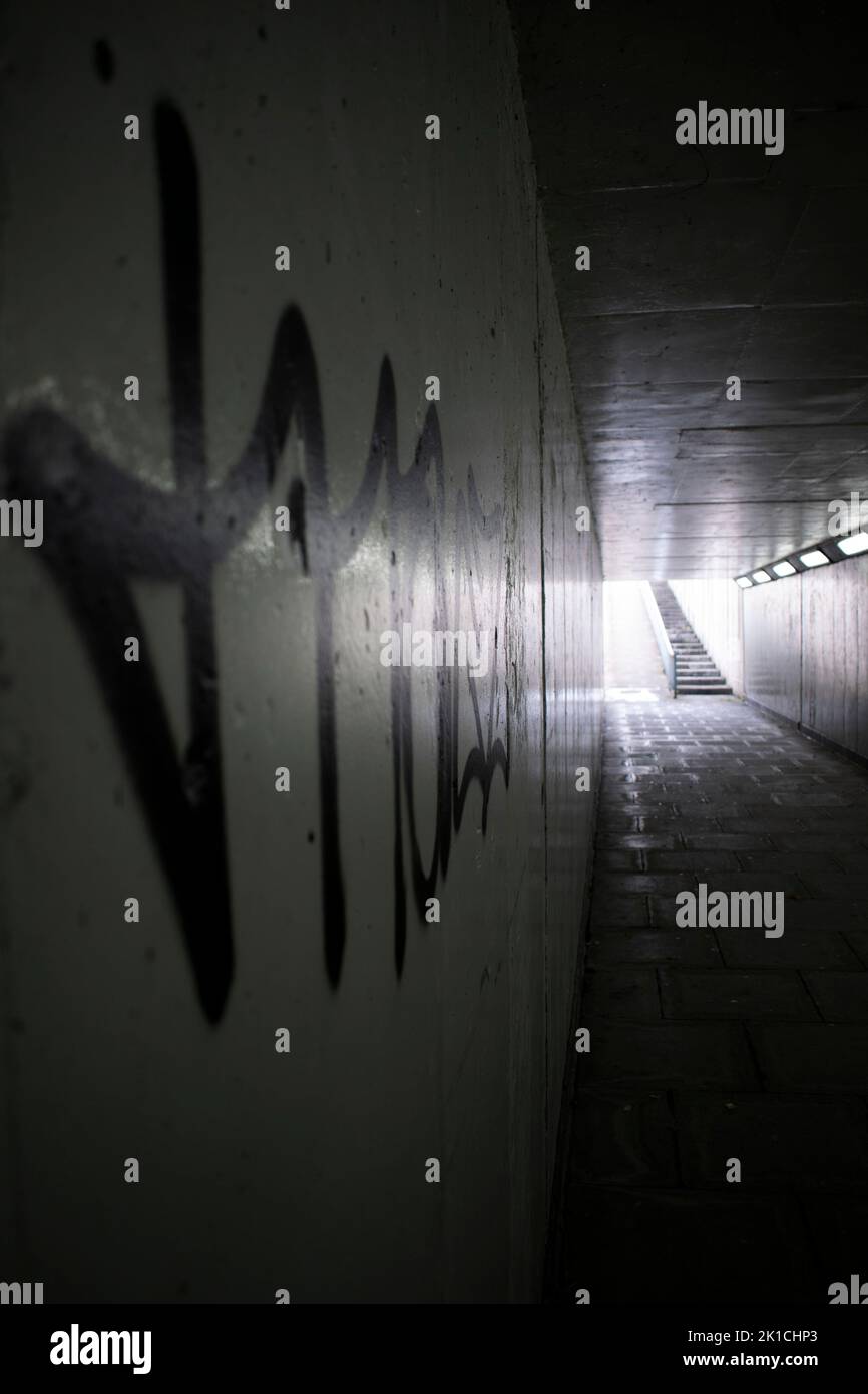 Eine dunkle Unterführung mit Licht am Ende des Tunnels und Graffiti an einer Wand Stockfoto
