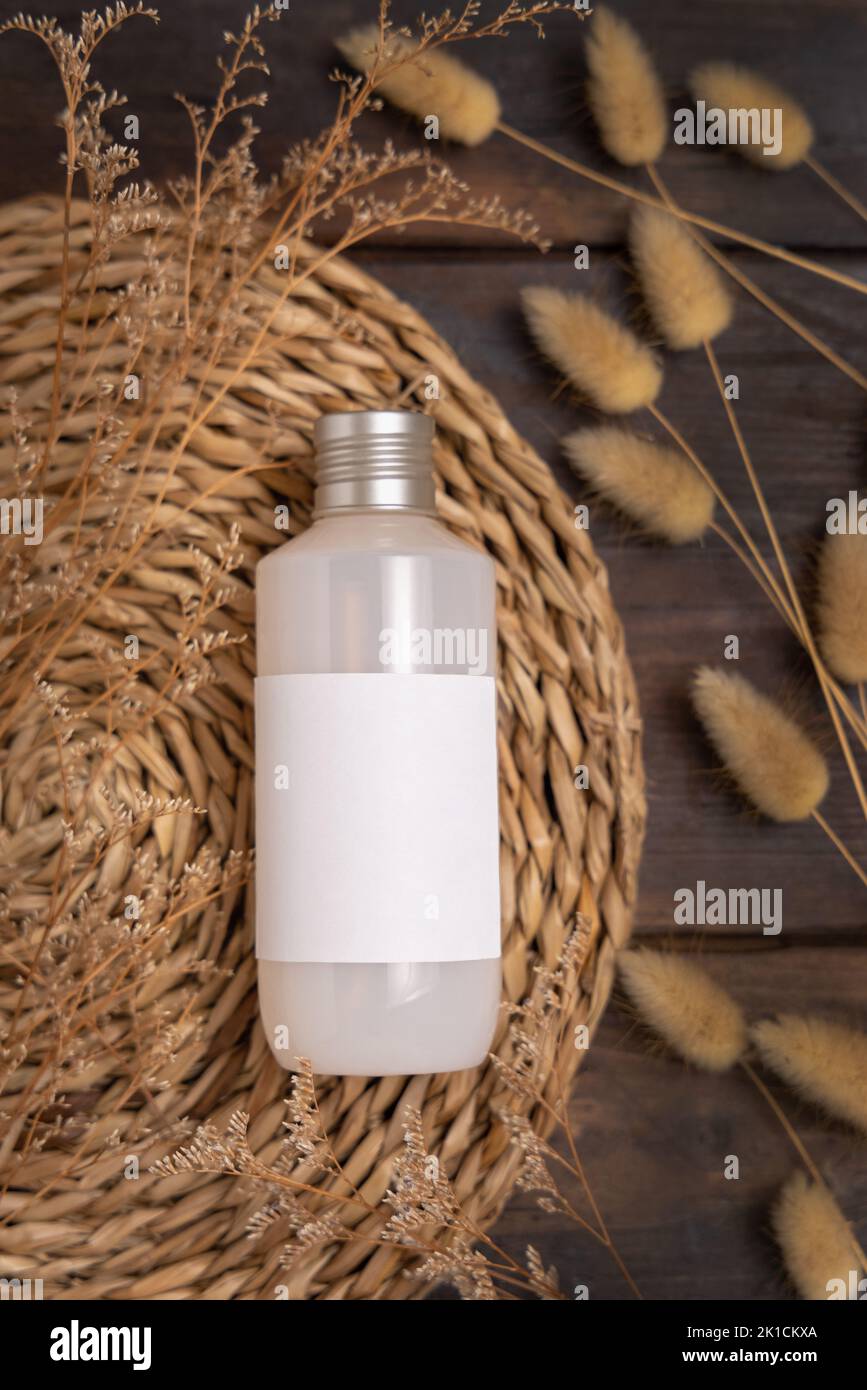 Kosmetikflasche auf Boho watschelte Tischset in der Nähe von Hare's Tail Grass Draufsicht auf Holz, Label-Mockup. Natürliches Hautpflegeprodukt, Creme oder Lotion. Böhmische ec Stockfoto
