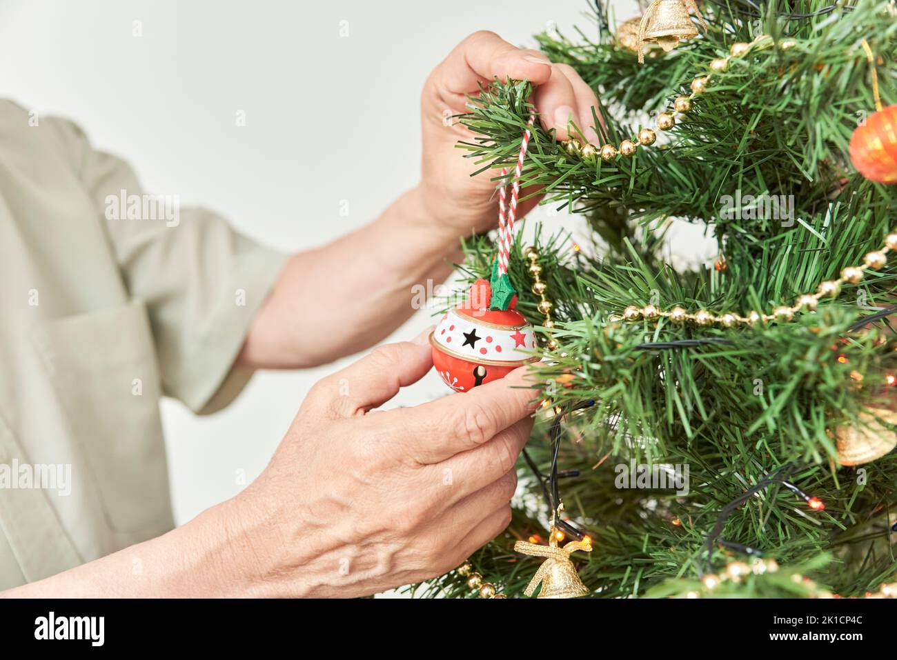 Nicht erkennbarer älterer Mann, der zu Hause einen Weihnachtsbaum schmückt, männliche Hände hängen einen Ball an einen Ast. Stockfoto