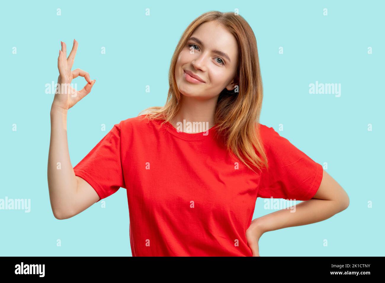 OK-Schild. Gut gemacht. Porträt einer zufriedenen freundlichen Frau in rotem T-Shirt ermutigend mit Zustimmung Hand Geste lächelnd isoliert auf blauem Hintergrund. De Stockfoto
