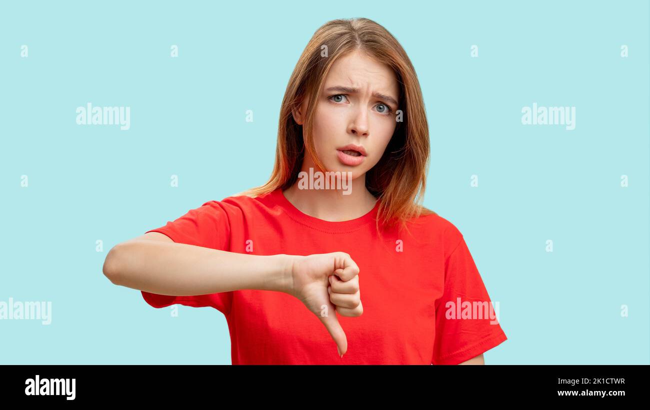 Geste nicht gefallen. Negative Antwort. Porträt einer verärgerten Skeptikerin im roten T-Shirt, die kritisiert, zeigt den Daumen isoliert auf blauem Hintergrund. Verlierer Stockfoto