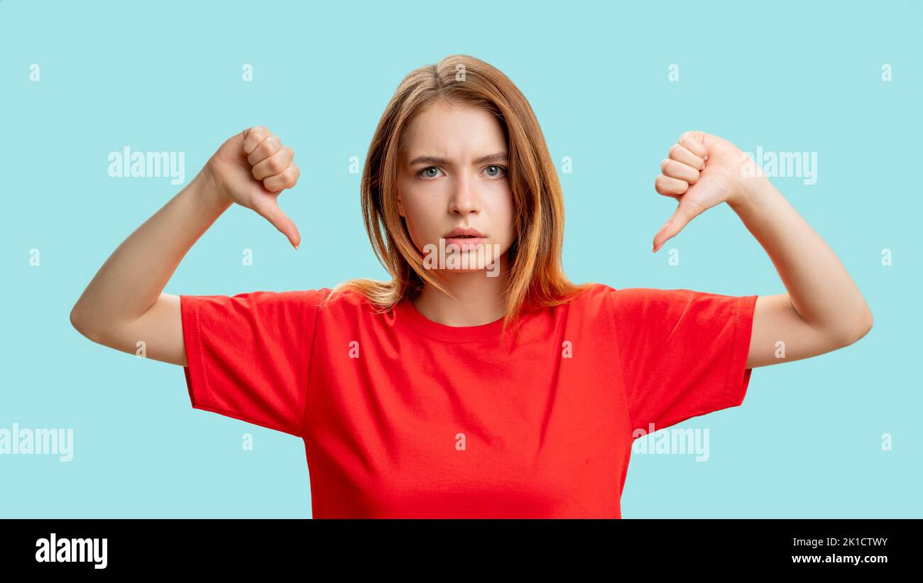 Mag Zeichen nicht. Geste der Meinungsverschiedenheit. Porträt einer gestörten Dame im roten T-Shirt, die mit den Daumen nach unten isoliert auf blauem Hintergrund protestiert. Negative Auswirkungen Stockfoto