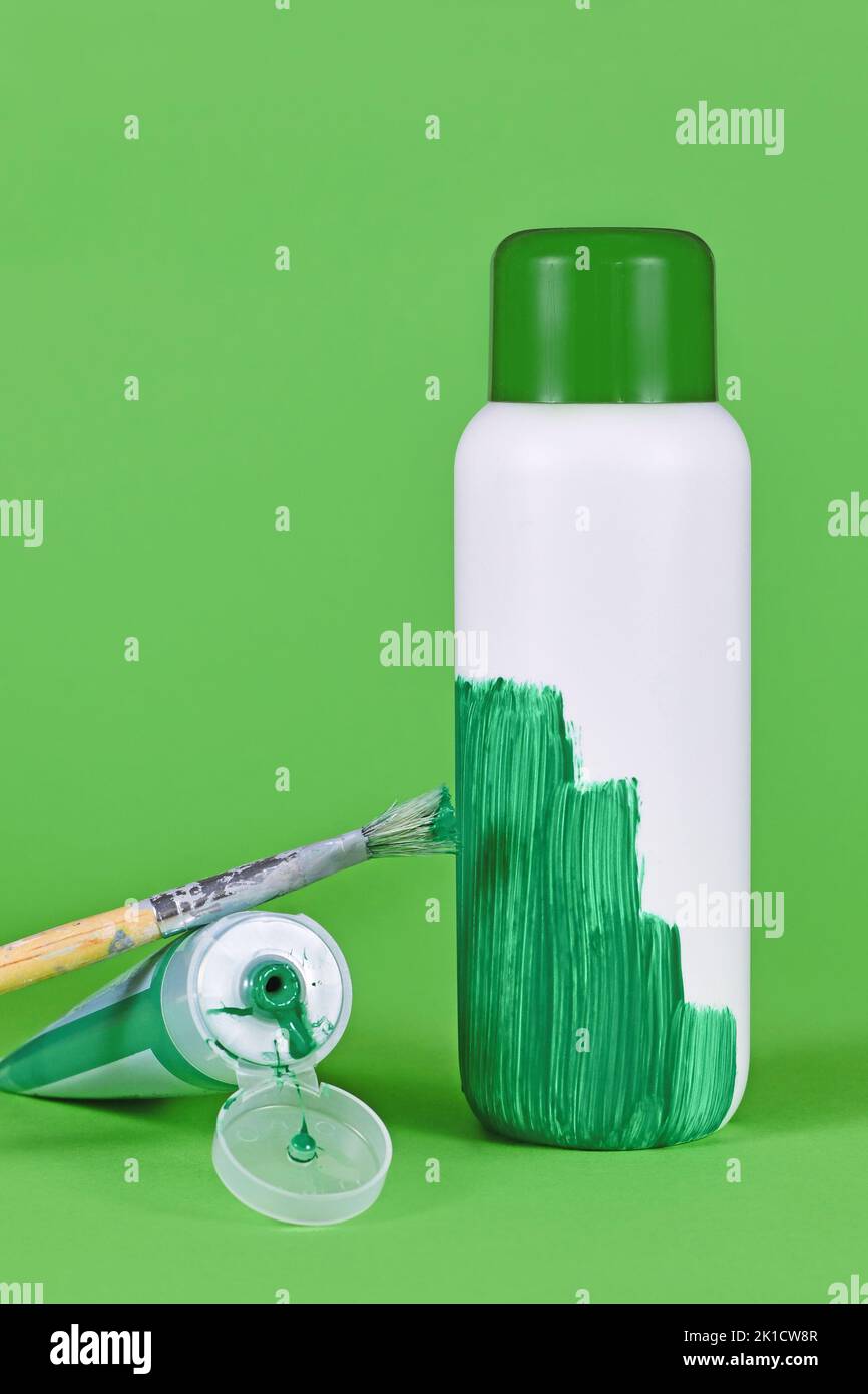 Greenwashing-Konzept mit weißer Plastikflasche, die grün lackiert wird Stockfoto