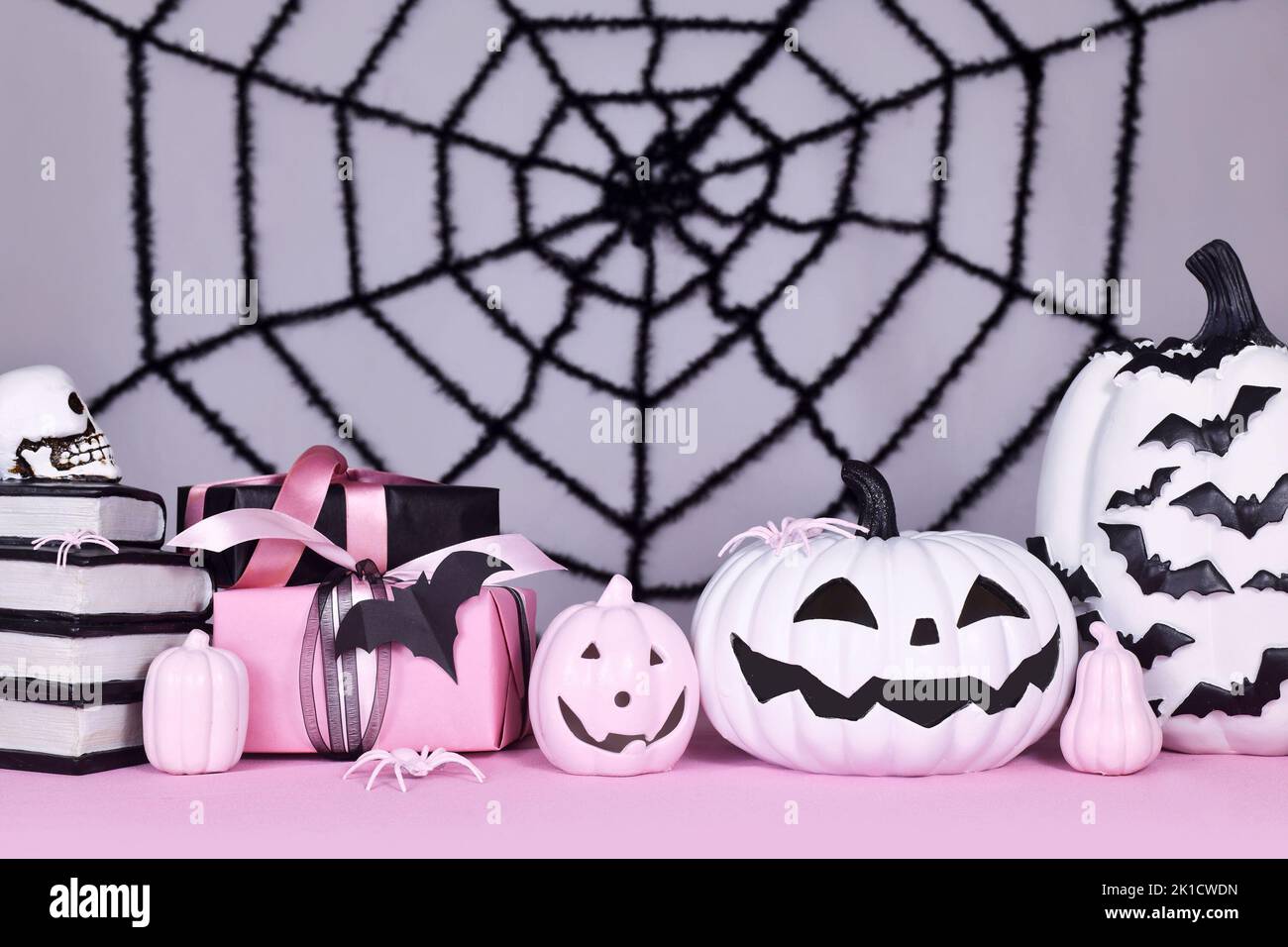 Pink-weißes Halloween Dekor mit schwarzen und weißen Kürbissen, Hexenhut und Zauberbüchern auf grauem Hintergrund mit riesigem Spinnennetz Stockfoto