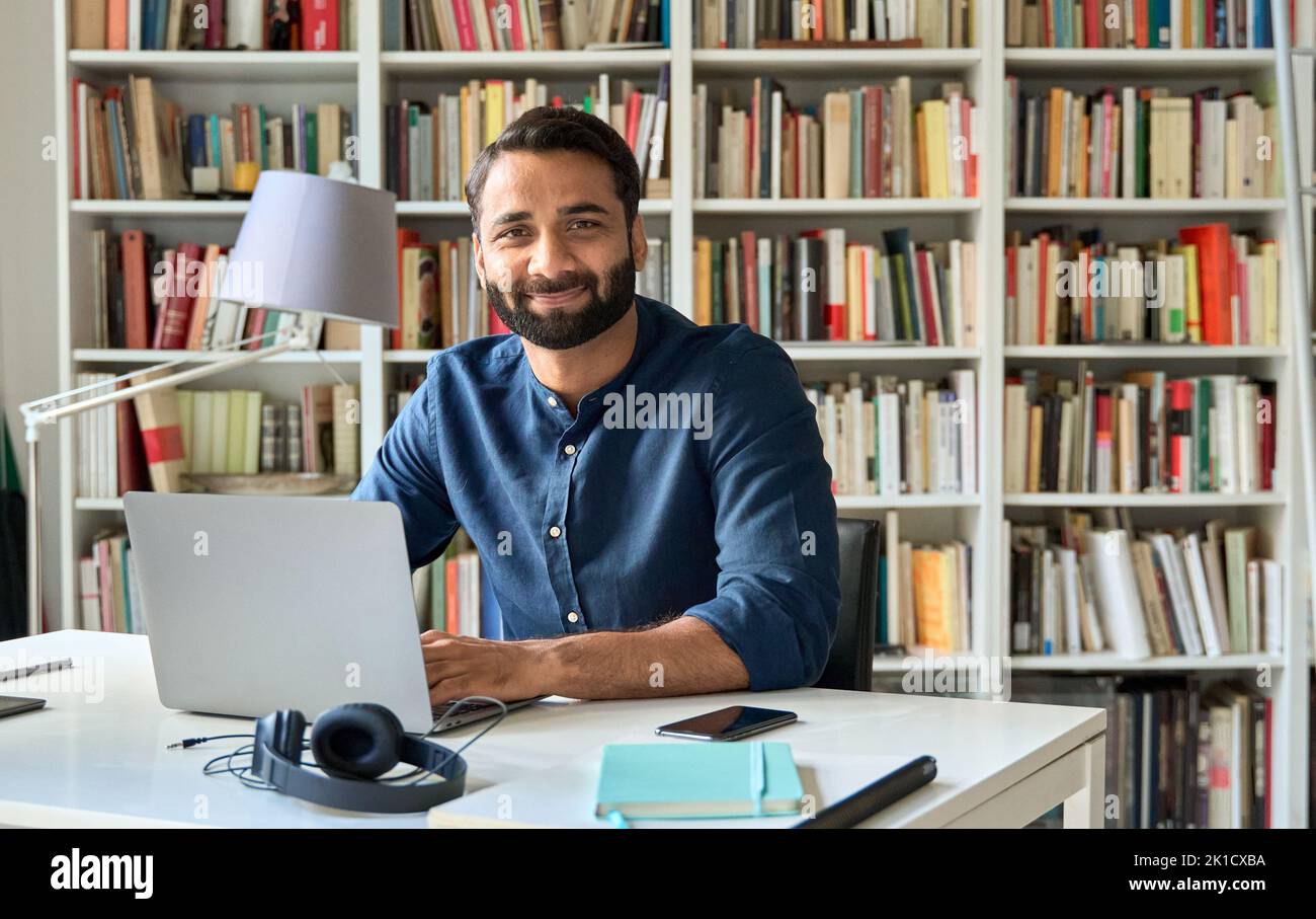 Glücklicher indischer professioneller Geschäftsmann, der bei der Arbeit mit einem Laptop sitzt, Porträt. Stockfoto