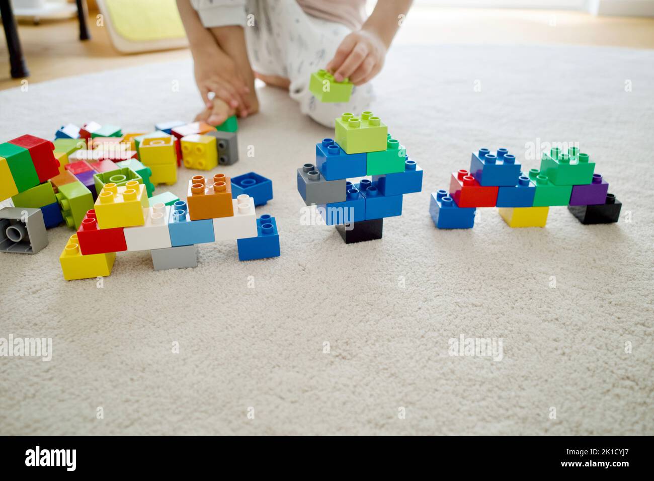 Ein Kind spielt auf einem weißen Teppich Bausteine. Es war tagsüber zu Hause. Stockfoto