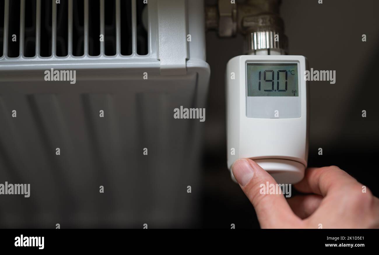 Hand dreht die Temperatur auf 19 Grad Celsius auf einem elektronischen Thermostat. Symbol für Energieeinsparung. Stockfoto