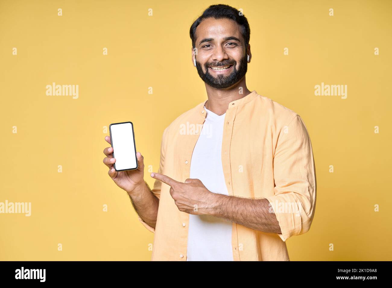 Glücklicher indischer Mann zeigt auf Mobiltelefon isoliert auf gelbem Hintergrund. Stockfoto