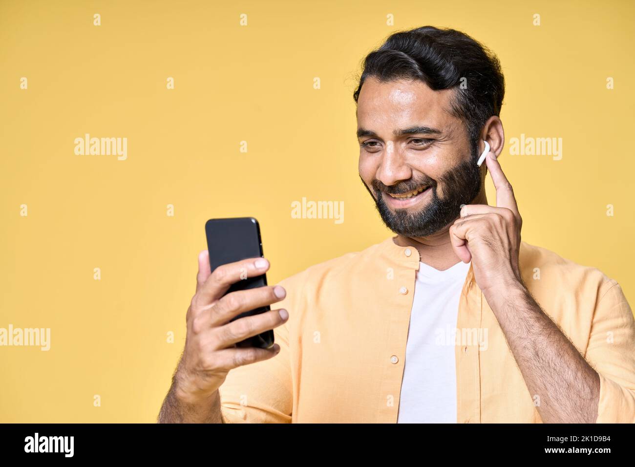 Glücklicher indischer Mann, der Ohrstöpsel mit Mobiltelefon trägt und Videoanruf führt. Stockfoto