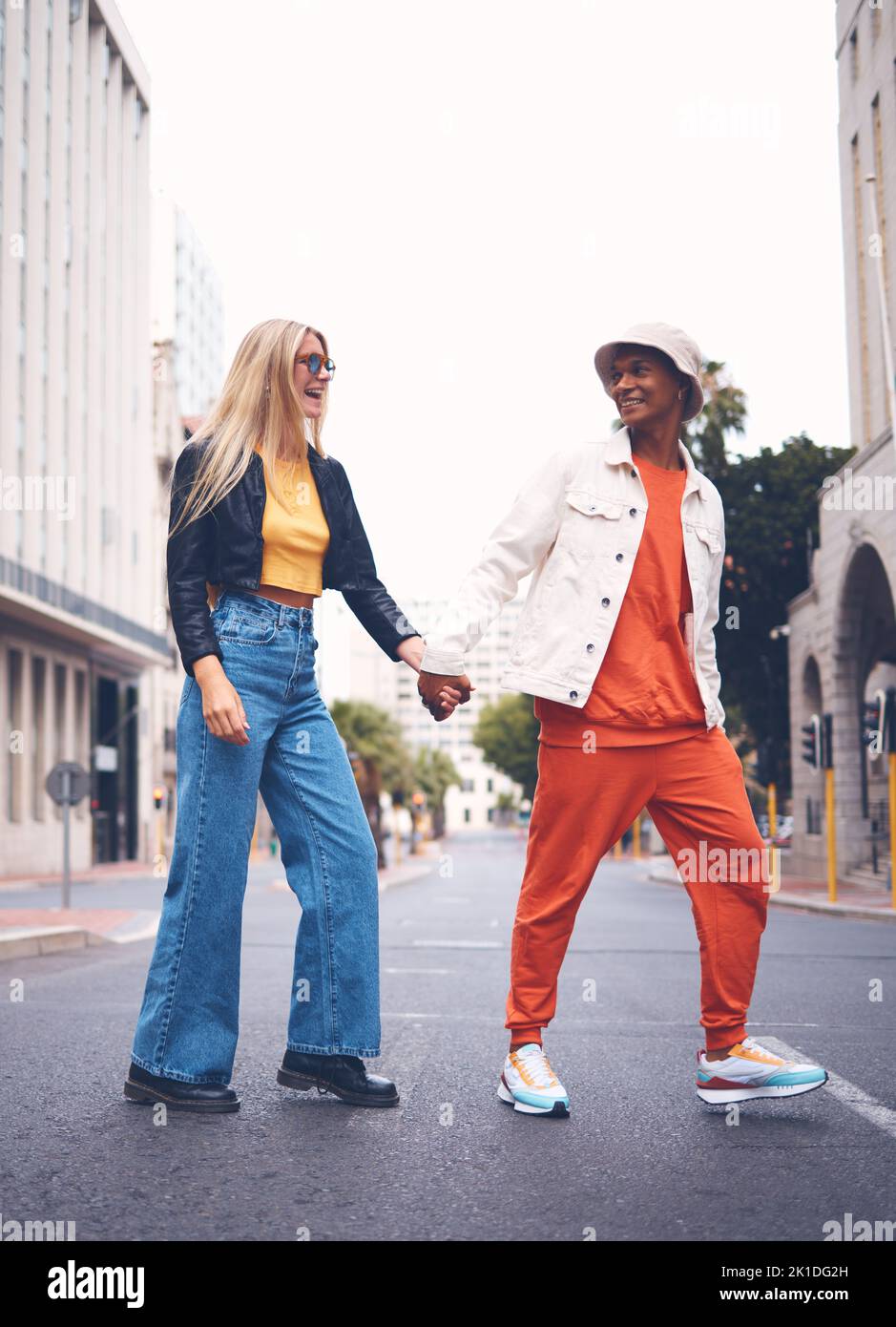 Glückliches interrassisches Paar mit Modebekleidung in einer städtischen Stadtstraße mit einem Lächeln und Liebe. Trendy, stylish oder Punk Mann und Frau zu Fuß in einer Stadt Stockfoto