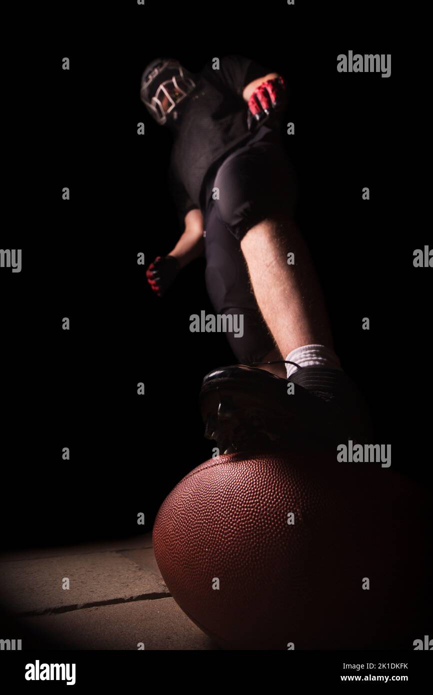 Mann in amerikanischer Fußballkleidung, der mit einem Fuß auf dem Ball steht. Stockfoto