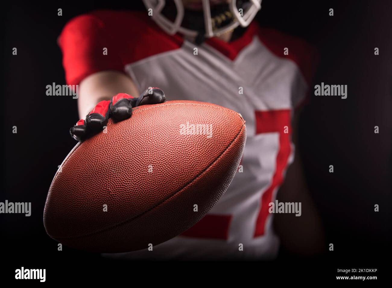 Mann in der Kleidung eines amerikanischen Fußballspielers, der den Ball zur Kamera hin aushält. Stockfoto