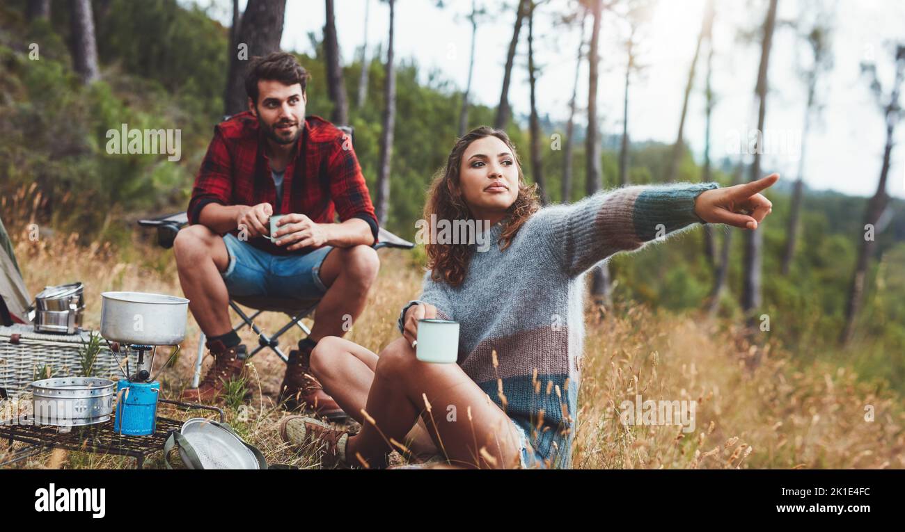 Junge Frau, die auf eine Richtung zeigt, während sie mit ihrem Freund kampt. Abenteuerliches junges Paar, das seinen Urlaub auf einem Campingplatz genießt. Stockfoto