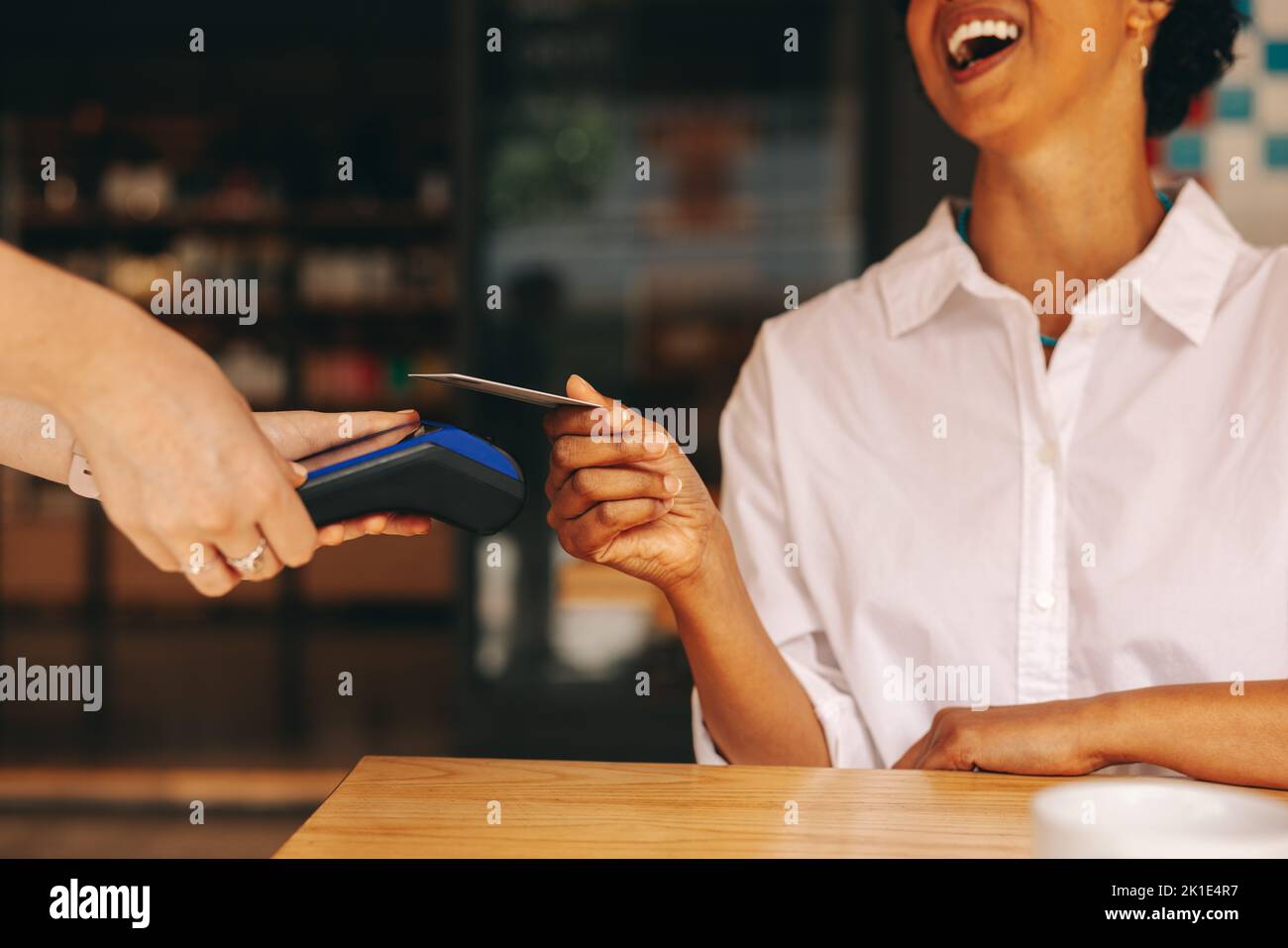 Glückliche Kundin scannt ihre Kreditkarte auf einem Kartenautomaten, um ihre Rechnung in einem Café zu bezahlen. Fröhliche Frau, die eine bargeldlose und kontaktlose Transaktion macht Stockfoto