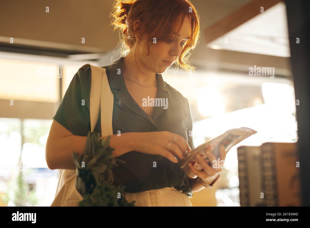 Kundin, die das Etikett eines Lebensmittelprodukts liest, während sie in einem Lebensmittelgeschäft steht. Junge Frau, die in einem trendigen Supermarkt Lebensmittel einkauft Stockfoto