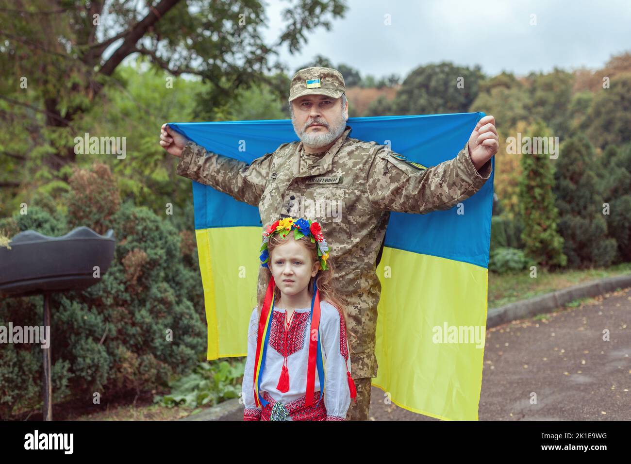 Porträt eines ukrainischen Soldaten mit seiner kleinen Tochter. Sie stehen mit der Flagge der Ukraine. Stockfoto