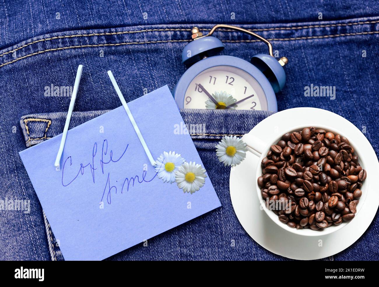 Blauer Wecker mit Kaffeebohnen Espresso-Tasse über Jeans oder Denimtaschen wie Concept Time und Liebe für Kaffee oder Morgenkaffee oder Kaffee t Stockfoto