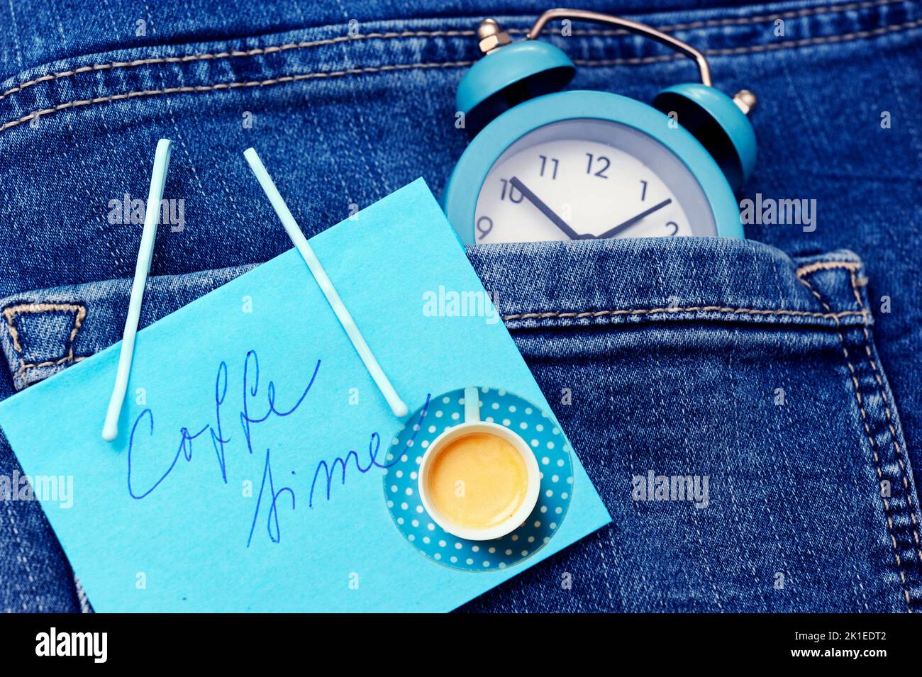 Blauer Wecker mit Kaffeebohnen Espresso-Tasse über Jeans oder Denimtaschen wie Concept Time und Liebe für Kaffee oder Morgenkaffee oder Kaffee t Stockfoto