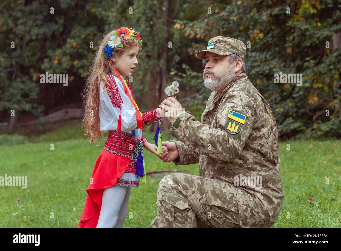 Ein kleines ukrainisches Mädchen in Nationalkostüm trifft ihren Vater aus dem Krieg. Stockfoto