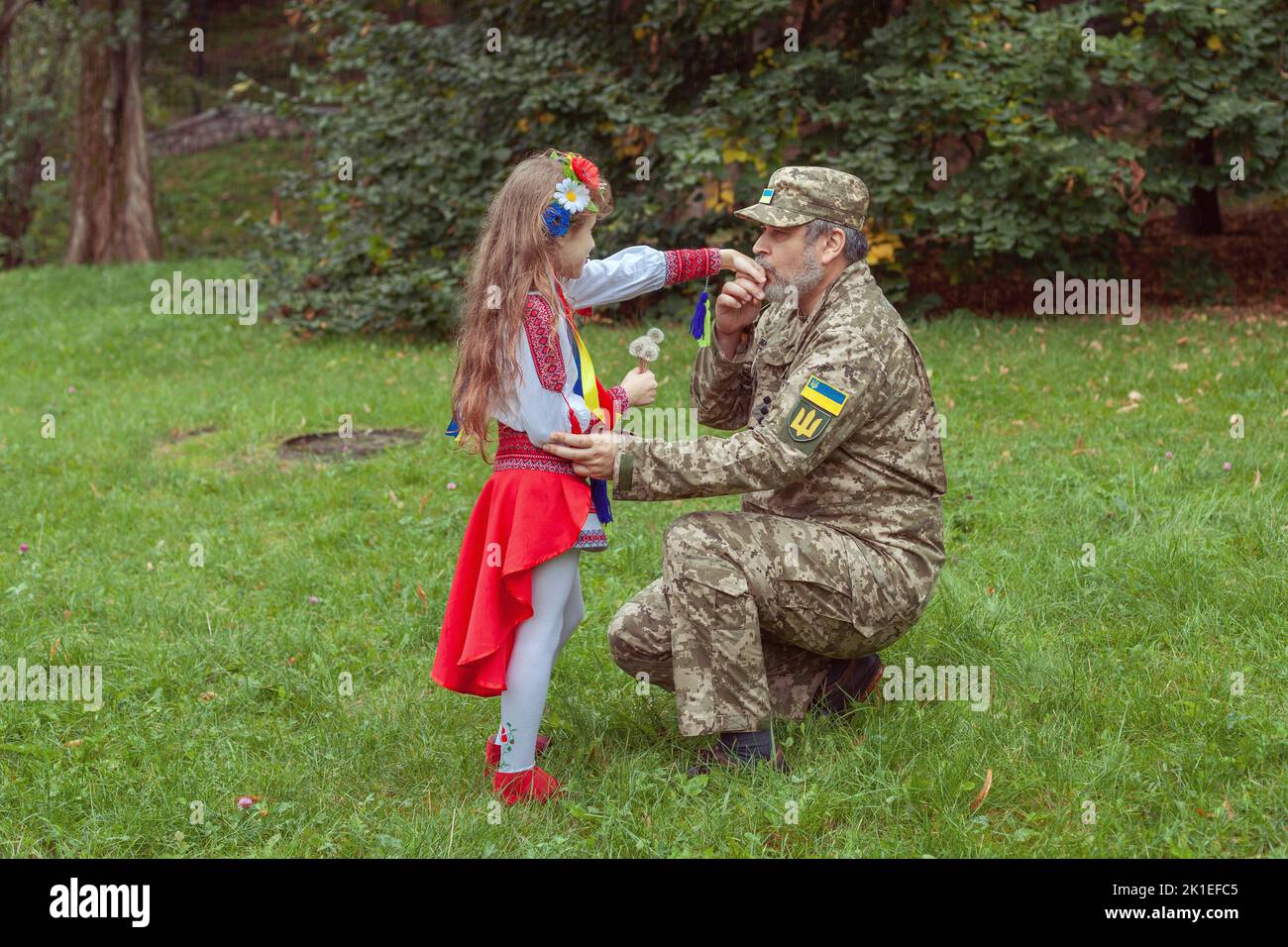 Ein kleines ukrainisches Mädchen in Nationalkostüm trifft ihren Vater aus dem Krieg. Stockfoto