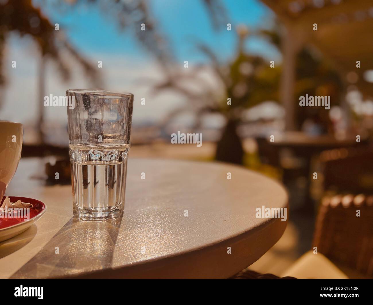 Ein halbes Wasserglas auf dem Tisch eines Open-Air-Cafés am Strand Stockfoto