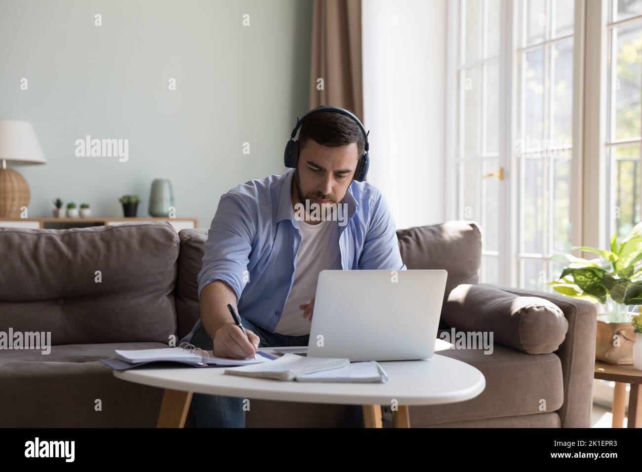 Konzentrierter Student im Alter von tausend Jahren, Mann in kabellosen Kopfhörern, der online studiert Stockfoto