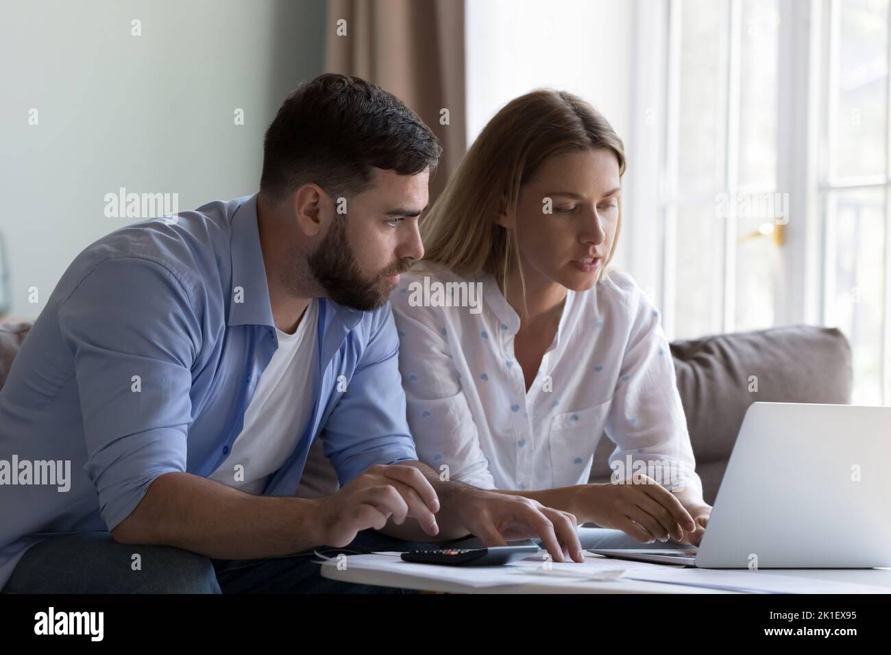 Seriöse fokussierte Ehefrau zeigt dem Ehemann eine Online-App für inländische Zahlungen Stockfoto