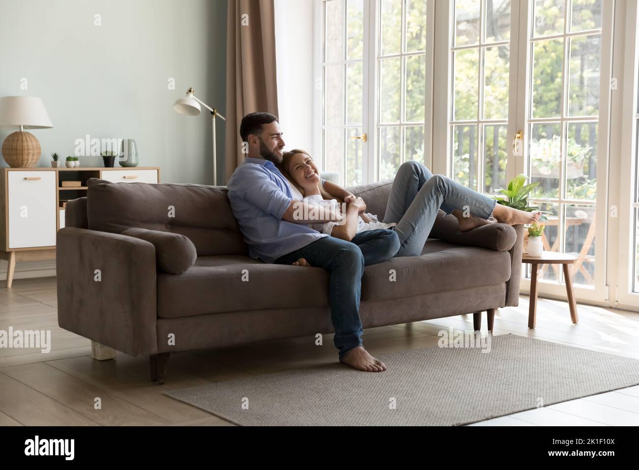 Glückliches junges Familienpaar, das sich auf einer bequemen Couch entspannt Stockfoto