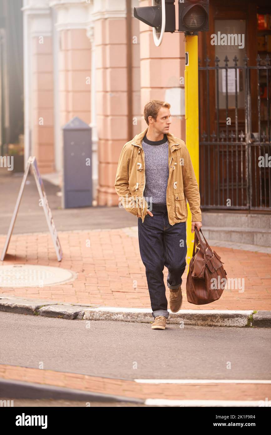 Weiter. Ganzkörperaufnahme eines modischen Mannes, der eine Straße in der Stadt überquert. Stockfoto