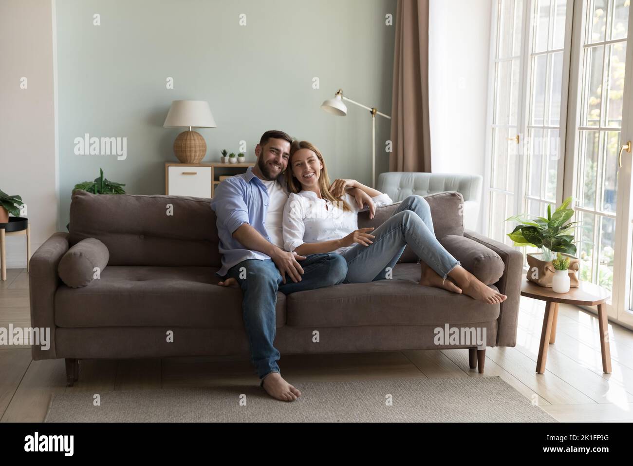 Glückliches junges, tausendjähriges Paar Hausbesitzer, die sich auf einem bequemen Sofa ausruhen Stockfoto