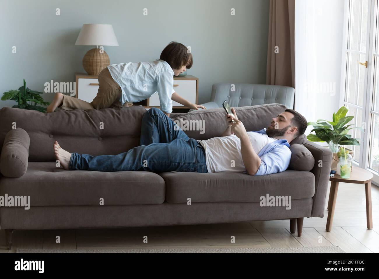 Entspannter Vater, der sich auf dem Sofa ausruht und das Mobiltelefon hält Stockfoto