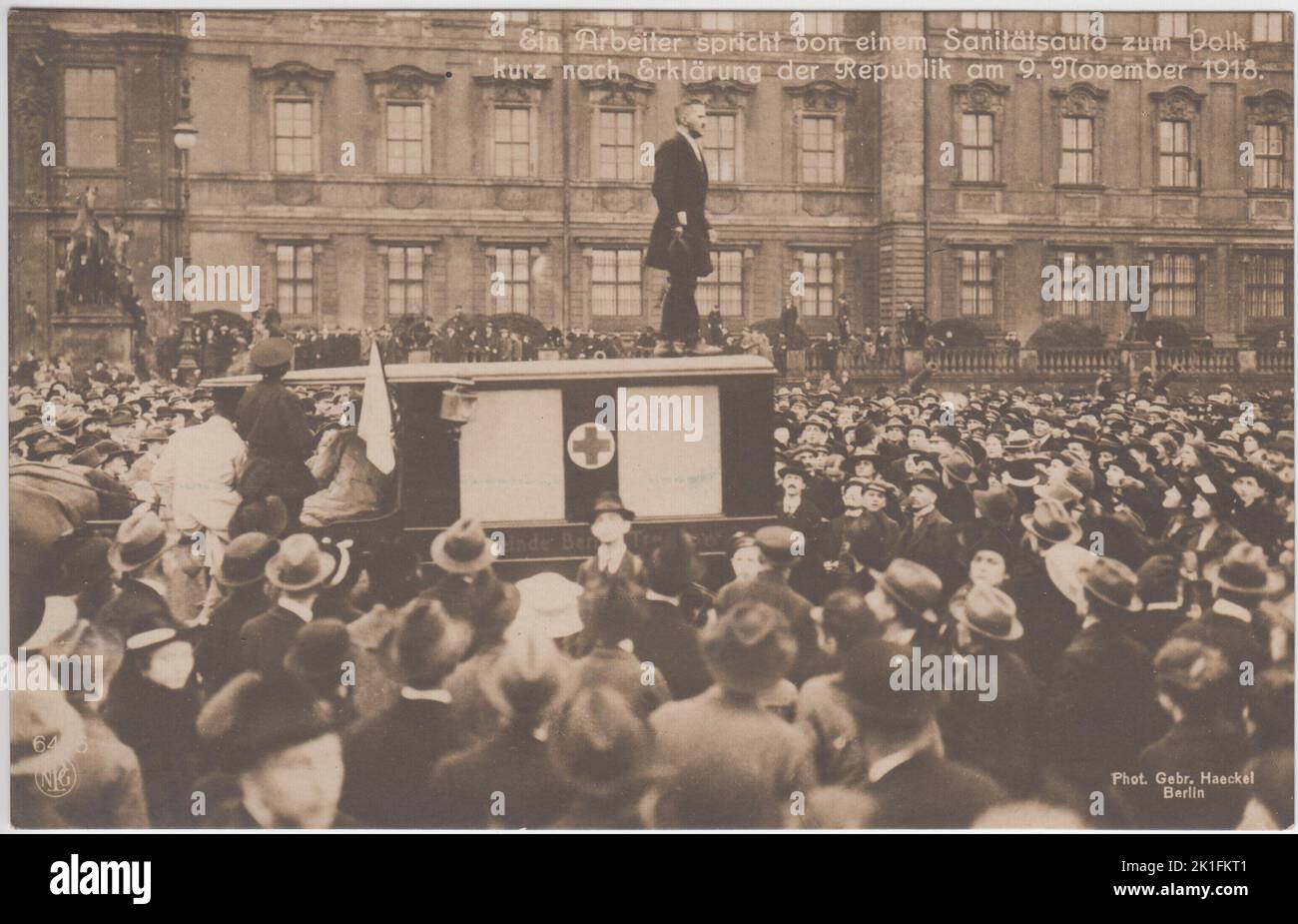 Ein Arbeiter spricht von einem Sanitätsauto zum Volk kurz nach Erkennung der Republik am 9. November 1918 / Ein Arbeiter spricht kurz nach der Erklärung der Bundesrepublik am 9. November 1918 von der Spitze eines Krankenwagens zu den Menschen. Postkarte von Gebr. Haeckel, Berlin, zeigt einen Redner, der auf einem Krankenwagen mit Pferdegezogenem steht und eine große Menschenmenge während der deutschen Novemberrevolution anspricht. Stockfoto