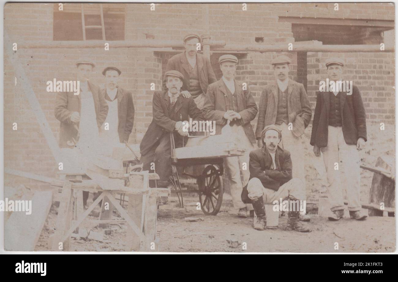 Plymouth Hausbauer bei der Arbeit im frühen 20.. Jahrhundert. Foto einer Gruppe von Männern in Arbeitskleidung (einschließlich flacher Kappen) auf einer Baustelle. Hinter ihnen ist ein teilweise konstruiertes Haus zu sehen. Werkzeuge, einschließlich Schubkarre und Säge, sind auf dem Foto zu sehen. Die Fotopostkarte wurde 1908 verschickt Stockfoto