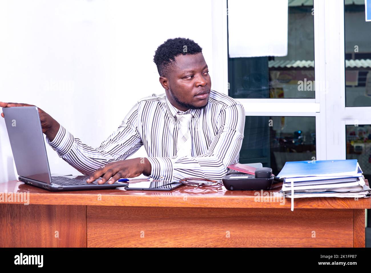 Ein junger Geschäftsmann in einem gestreiften Hemd, der in einem Büro sitzt und an einem Laptop arbeitet Stockfoto