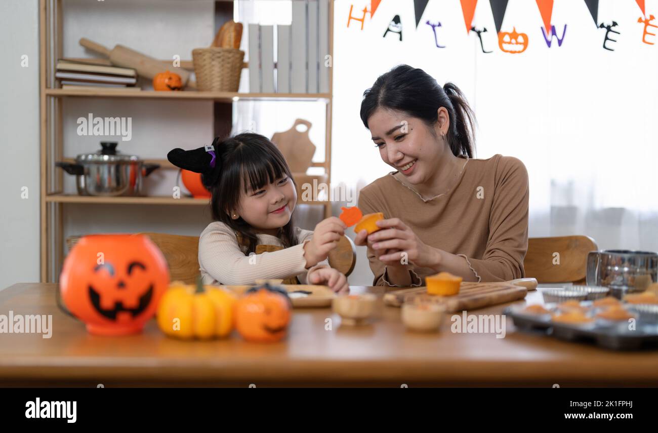 Glücklich lächelnde Familie Mutter und Tochter machen Halloween-Home Dekorationen zusammen, während sie am Holztisch sitzen. Stockfoto