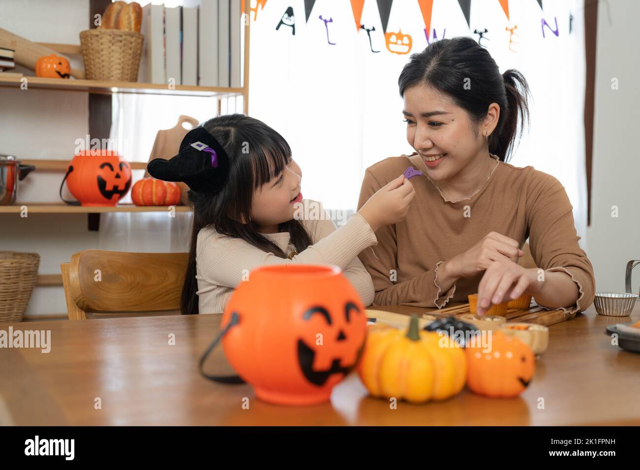 Glücklich lächelnde Familie Mutter und Tochter machen Halloween-Home Dekorationen zusammen, während sie am Holztisch sitzen. Stockfoto