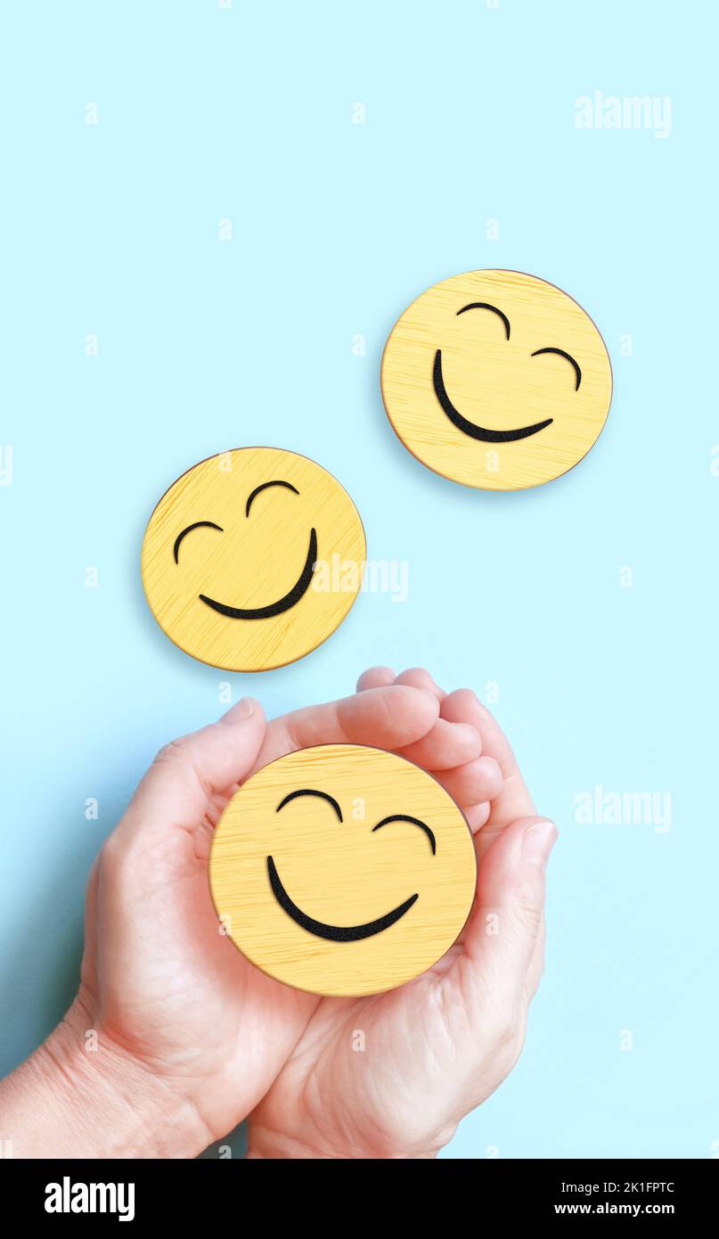 Hand hält glückliches Lächeln Gesicht auf blauem Hintergrund, positives Denken, psychische Gesundheit, Welt psychische Gesundheit Tag Konzept Stockfoto