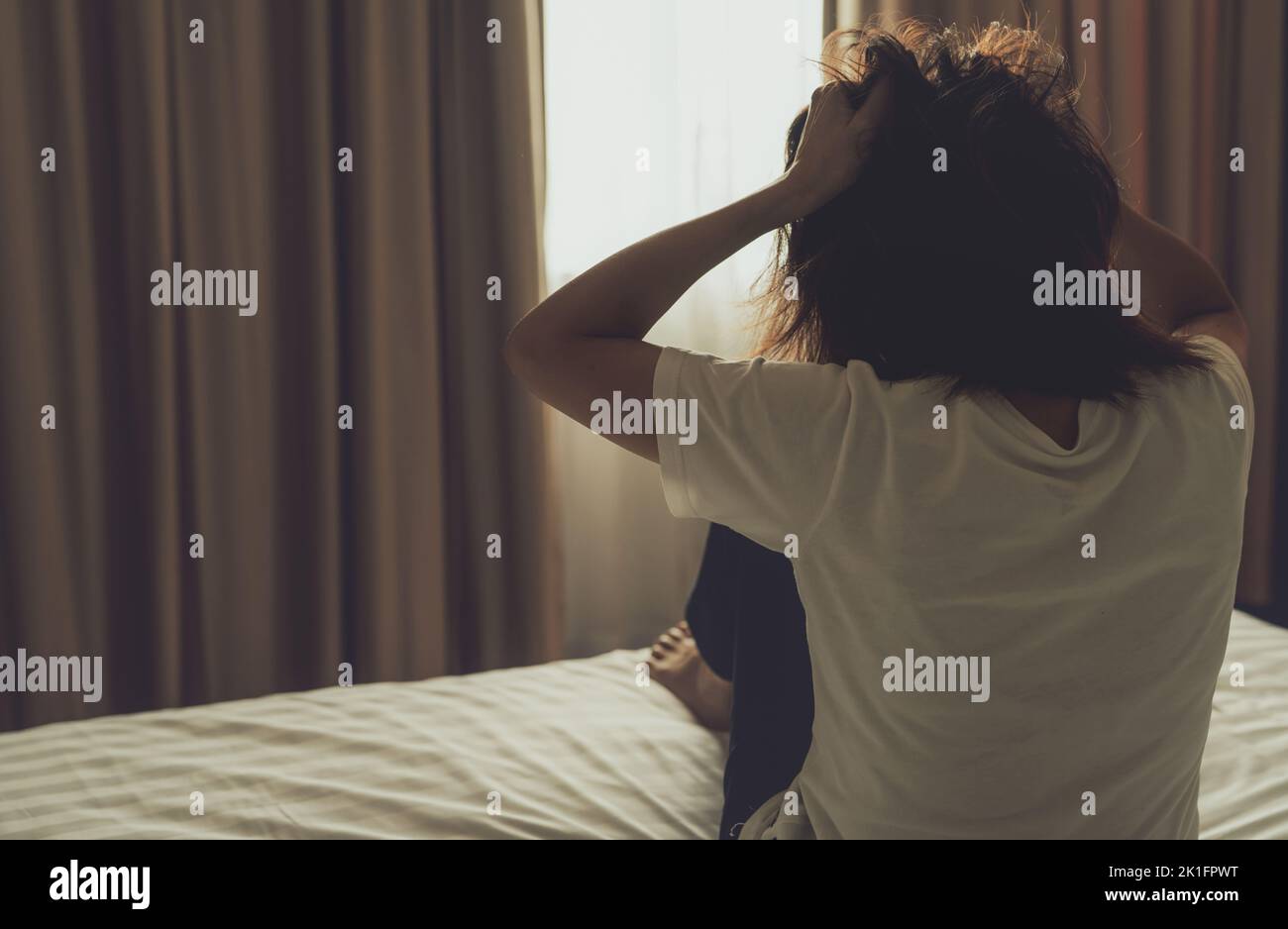 Konzept zum Welttag der psychischen Gesundheit. Rückansicht einer wütenden Frau, die Hand auf den Kopf legte und an den Haaren zog. Psychische Erkrankung Frau sitzt im Schlafzimmer auf dem Bett. Frau Stockfoto