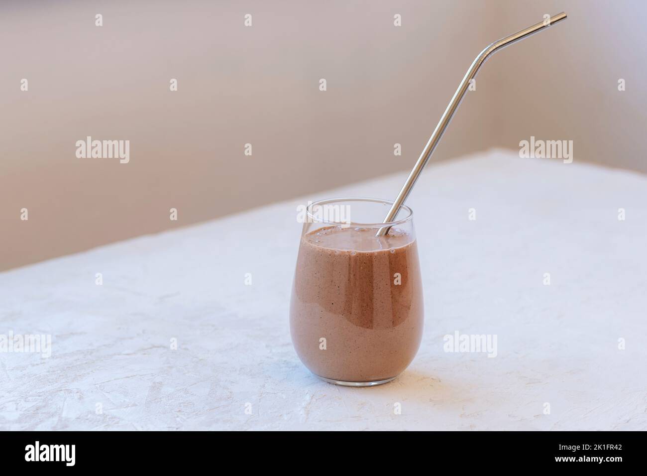 Protein-Schokolade-Smoothie mit Metallstroh auf weißem Tisch, Nahaufnahme. Stockfoto