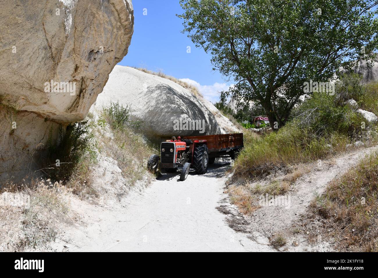 Ein roter Traktor auf einem schmalen Sandweg zwischen Felsen in der Landschaft in Kappadokien, Türkei Stockfoto