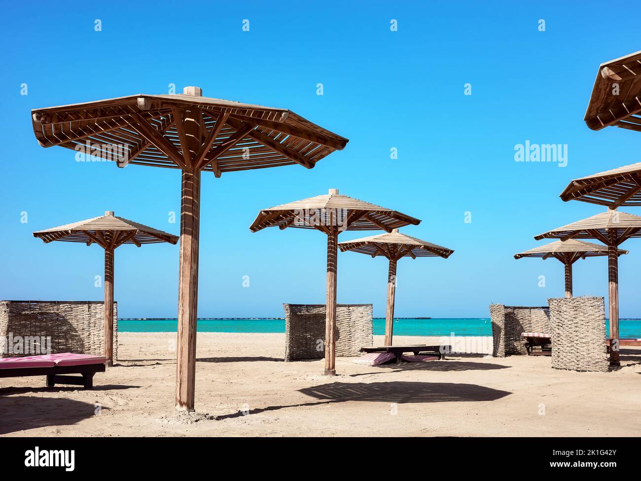 Hölzerne Sonnenschirme, Sonnenliegen und Windschutzscheiben am Strand, Marsa Alam, Ägypten. Stockfoto